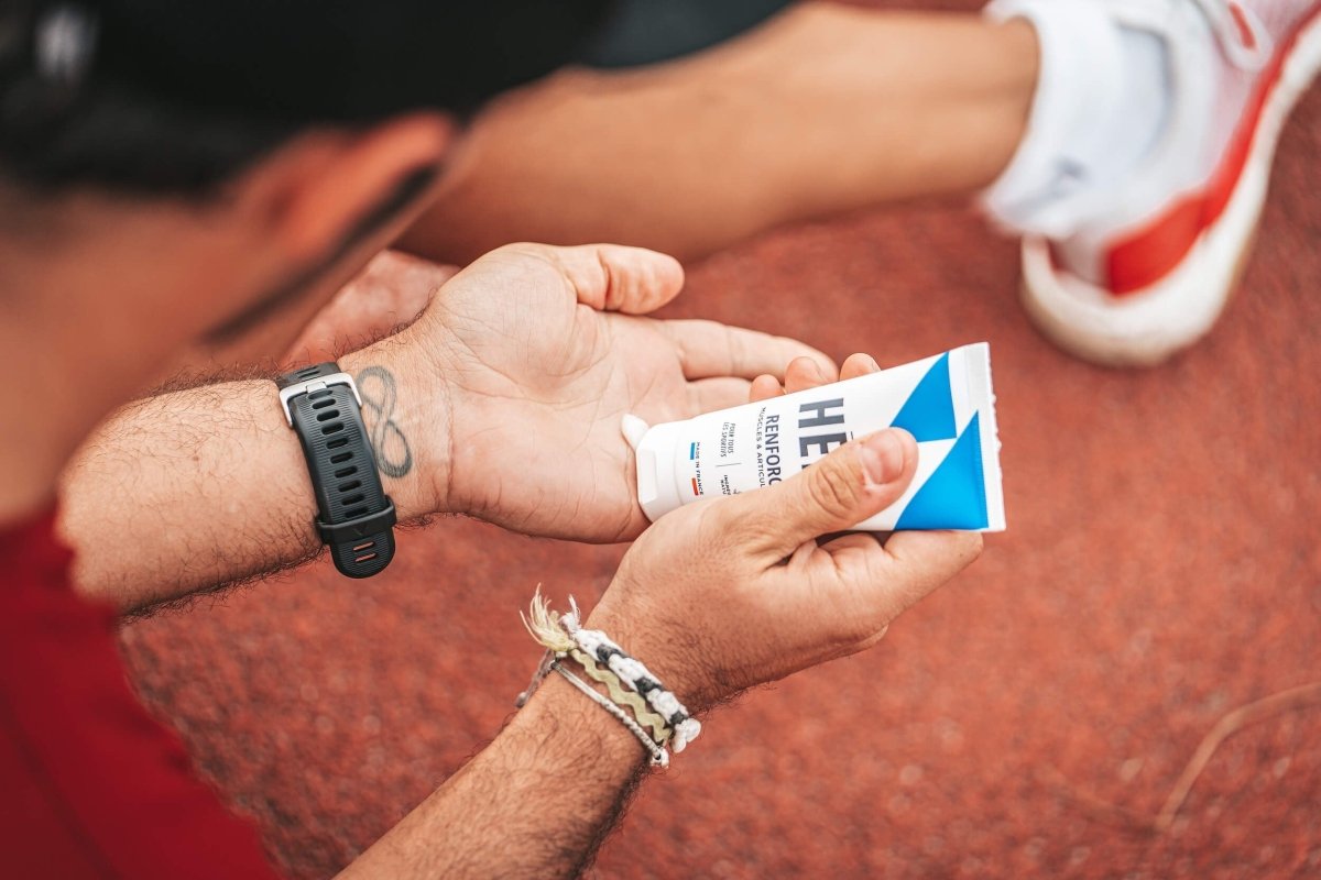 Sportif assis sur une piste d'athlétisme en train d'appliquer du gel articulaire Renforcer dans ses mains