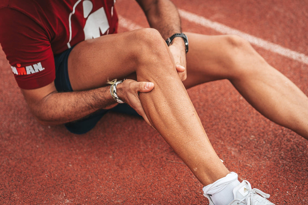 Sportif assis sur une piste d'athlétisme en train de se faire un massage sportif des mollets
